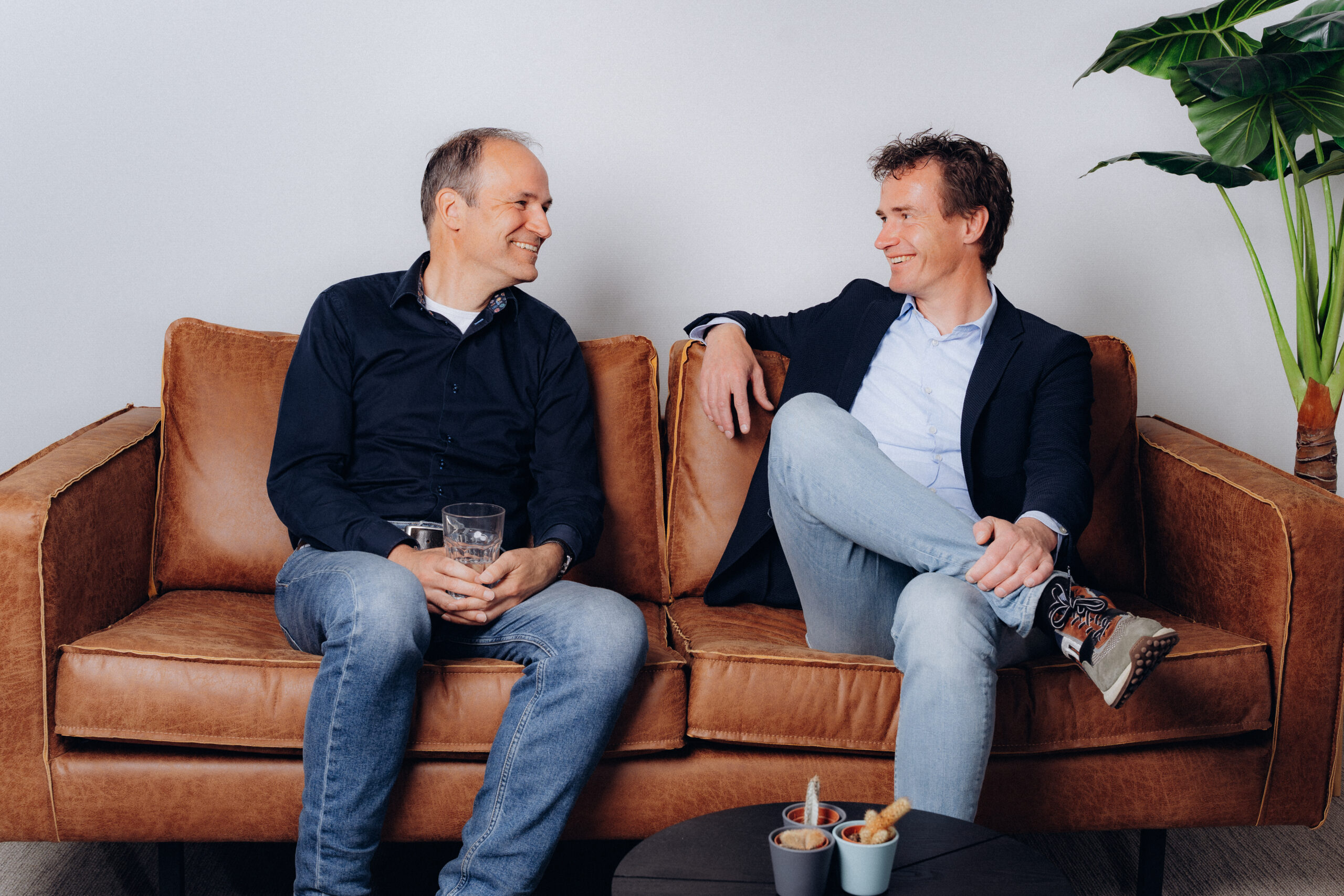 Twee Midglas collega's die met elkaar lachend een gesprek voeren op de bank