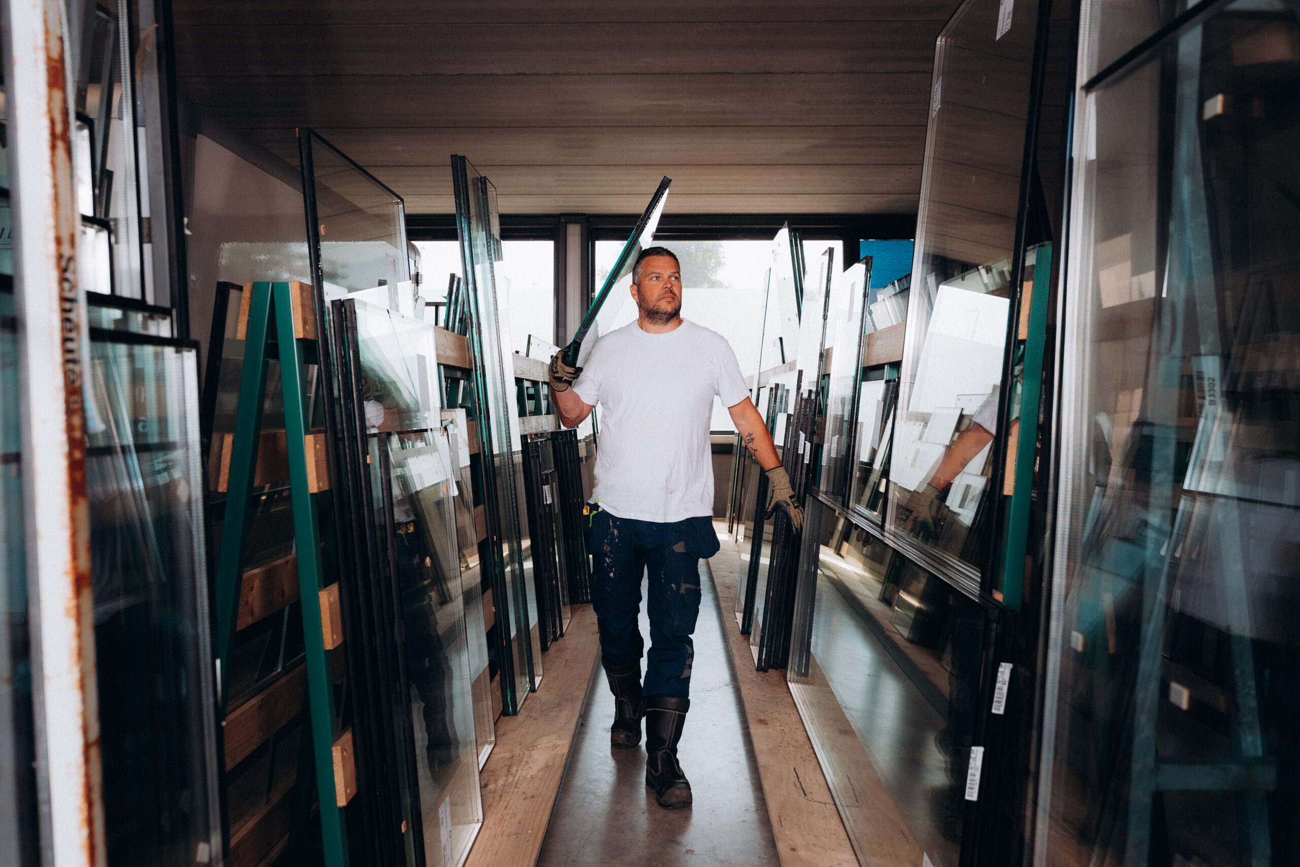 Glashersteller met een stuk glas op zijn schouder lopend door een glashal