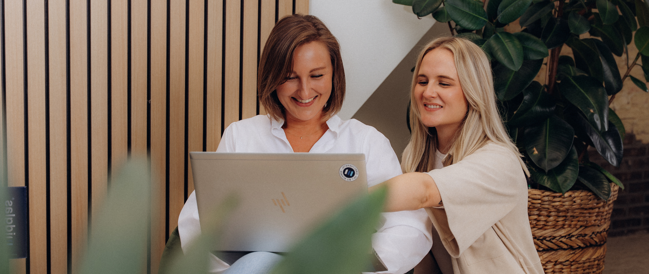 Twee lachende vrouwelijke collega's die samen op een laptop kijken