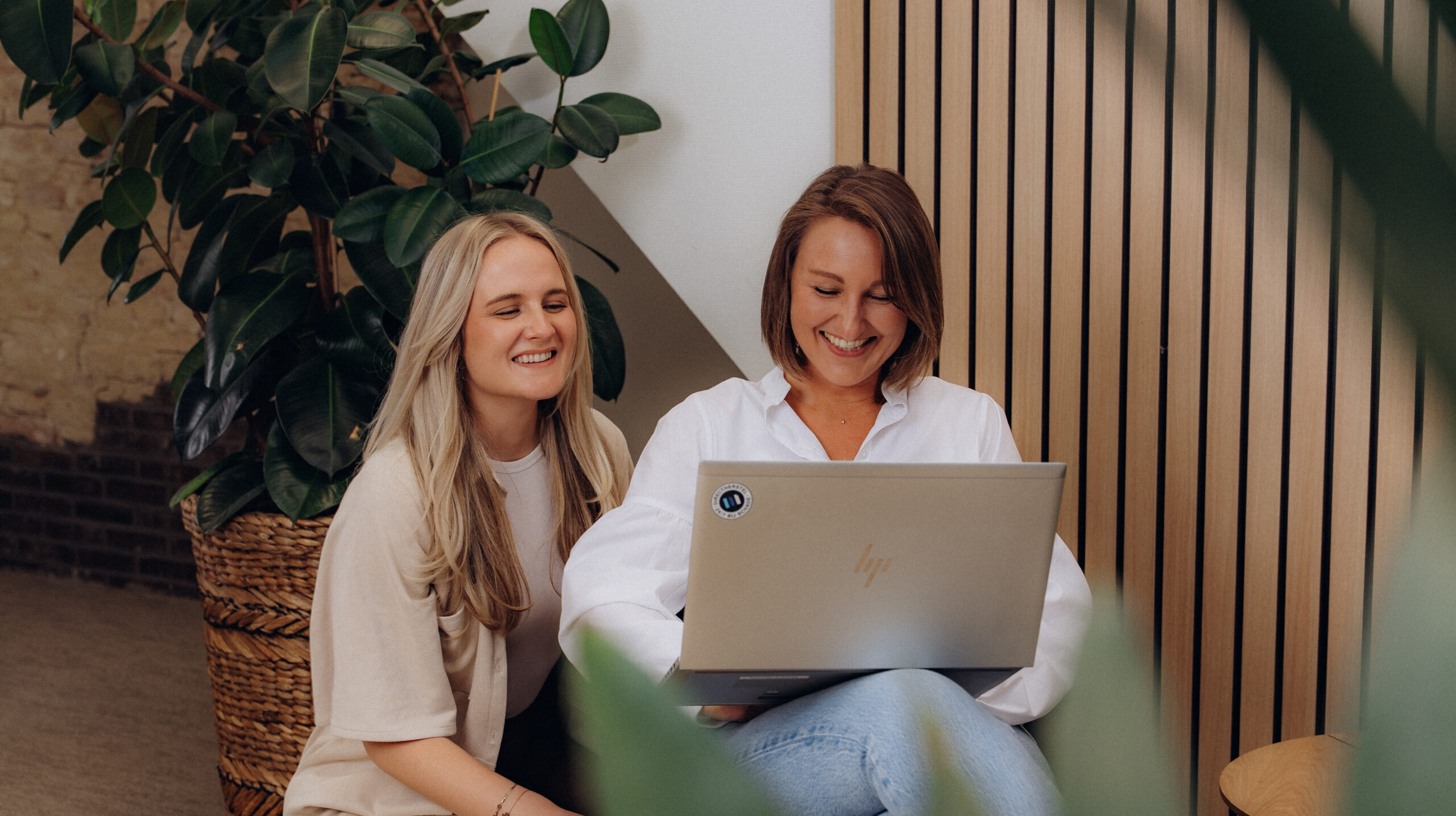 Twee lachende vrouwelijke collega's bij Midglas die samen op een laptop kijken
